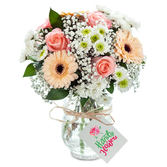 Carefully arranged with a fine eye for detail, this radiant bouquet is a fitting tribute to Norbiton's blend of urban vibrancy and leafy tranquility. Central to the arrangement are plump, peachy-pink roses, each petal unfurling in tight, gentle spirals that hint at timeless romance. Flanking these are two polished peach-orange gerbera daisies, their wide-set petals and dramatic brown centers forming cheerful focal points that reflect the community's welcoming spirit near Kingston Road. Between the main blooms, clusters of snowy white chrysanthemums-each with a delicate green eye-provide a lush, inviting texture reminiscent of Norbiton's well-kept gardens. Billowy tufts of baby's breath nest among the flowers, infusing the display with airy volume and softening the palette for a dreamy effect. Sprigs of rich green eucalyptus rise from the bouquet, adding subtle scent and grounding the softer tones with nature's own vitality. The clear glass vase tapers gently at the neck, its transparency allowing the viewer to admire each carefully aligned stem in its fresh water, while a neat bow of natural raffia or twine is tied around its rim. Hanging from this is a crisp white tag whose blank surface invites a message for any of life's milestones. Professionally photographed under gentle, even lighting, this arrangement is an elegant choice for birthdays, anniversaries, or simply letting loved ones know they're cherished within the heart of Norbiton.